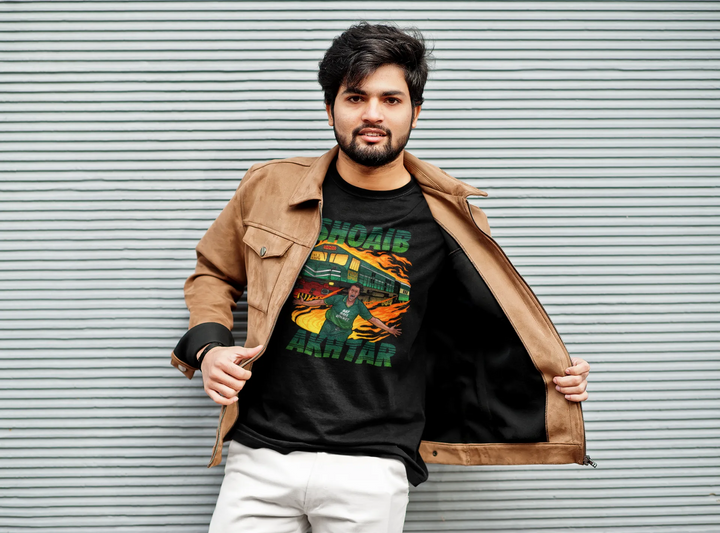 Fashionable young man standing against a striped metal background, wearing a tan leather jacket open to reveal a T-shirt with a vibrant graphic of cricketer Shoaib Akhtar in action, set against a fiery and dynamic background.