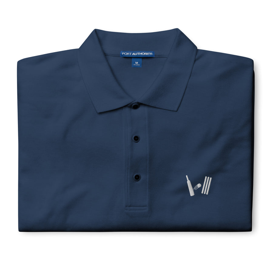 Close-up of the folded navy blue polo shirt highlighting the detailed embroidery of the cricket-themed logo on the left chest area.