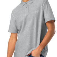 Casual grey polo shirt worn by a man, featuring a neat white embroidery of a cricket bat and stumps on the left chest, paired with blue jeans